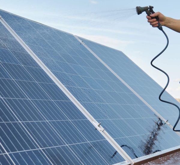 unrecognizable-technician-cleaning-solar-panels-with-water